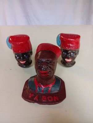 trois figurines représentant des hommes noirs coiffés de chapeaux rouges