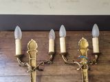 three brass wall sconces on a wooden table with a white wall