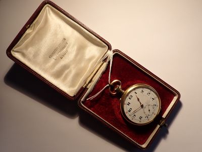 une montre de poche en or dans un écrin rouge, posée sur une table