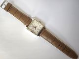 une image d'une montre sur une surface blanche avec un bracelet marron
