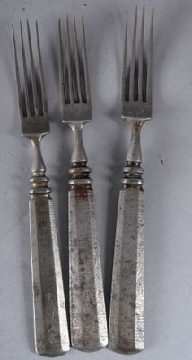 trois fourchettes et un couteau sont posés sur une surface blanche