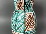 a green and brown vase sitting on a gray surface