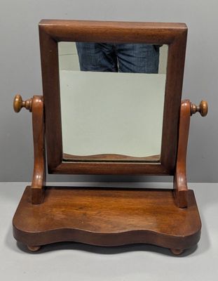 un petit miroir en bois posé sur un support, avec une personne debout à l'arrière-plan