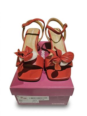 une paire de sandales rouges à talons hauts ornées d'un nœud, posée sur une boîte rose