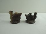 two figurines of birds sitting on a white surface