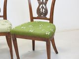 two wooden chairs with green upholstered cushions and a white wall