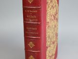 an old red book with gold trim sitting on top of a white surface