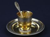 une tasse en argent contenant une cuillère, posée sur une assiette en argent