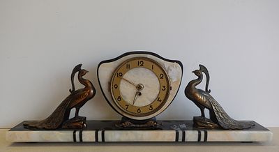 une horloge posée sur une étagère, surmontée de deux oiseaux