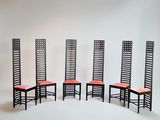 quatre chaises noires avec des coussins rouges sont adossées à un mur blanc