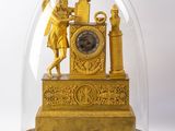 a gold clock under a glass dome on a wooden stand