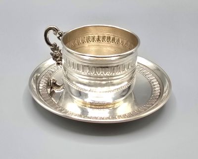 a silver cup and saucer sitting on a saucer