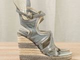 silver wedged sandal sandals on a wooden surface with a curtain in the background