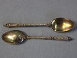 two silver spoons with ornate designs on them sitting on a table