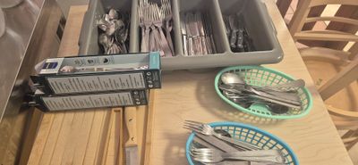 a tray of silverware on a table with a basket of forks and spoons