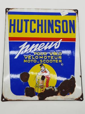 une vieille enseigne en tôle faisant la promotion de l'huile moteur Hutchinson, accrochée à un mur blanc