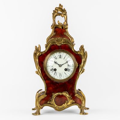 une horloge rouge et dorée posée sur une surface blanche