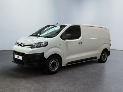 La camionnette blanche est garée dans une grande pièce au sol noir.