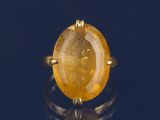 une image représentant une bague ornée d'une pierre jaune sur un fond noir