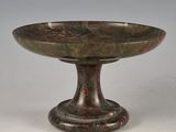 un bol ancien en bronze posé sur un socle, sur une surface blanche