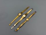 trois montres en or posées sur une surface grise, avec un fond gris