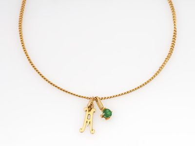 un collier plaqué or orné d'une pierre verte et d'un pendentif en forme d'initiale