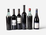 six bottles of wine are lined up in a row on a white surface
