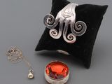 une photo d'une bague en argent sertie d'une pierre orange, posée sur un coussin