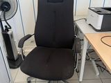 a black office chair sitting in front of a desk with a fan
