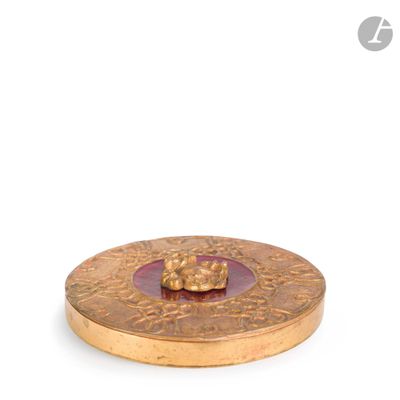 une assiette dorée avec un verre rose au centre, posée sur un fond blanc