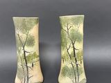 pair of vases with trees painted on them sitting on a table