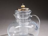 a glass teapot with a gold lid on a table