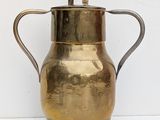 a gold pitcher with a handle on a white surface
