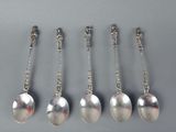six silver spoons with chains hanging from them on a gray surface