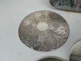four silver plates with designs on them on a table