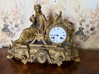 a gold clock sitting on a wooden table in front of a floral wallpaper