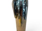 a silver vase that is on a stand on a white surface