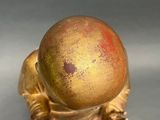 a gold figurine with a red ball on top of it