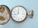 a small silver pocket watch sitting on a blue surface