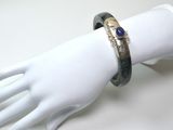une main de mannequin blanche tenant un bracelet orné d'une pierre bleue