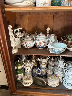 une vitrine en bois sur laquelle sont disposées de nombreuses pièces de vaisselle en porcelaine de styles variés