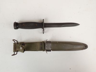 une paire de couteaux militaires posés sur une surface blanche, dont l'un se trouve au milieu des autres