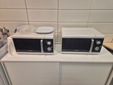 two microwaves sitting on top of a white cabinet