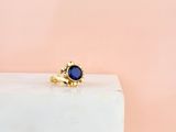 une bague en or sertie d'une pierre bleue repose sur un bloc de marbre