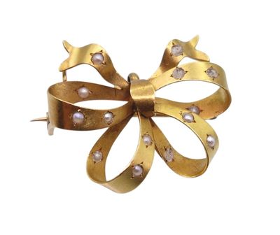 une image représentant une broche en forme de nœud en or ornée de perles