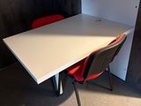 une table blanche avec deux chaises rouges dans un coin de la pièce