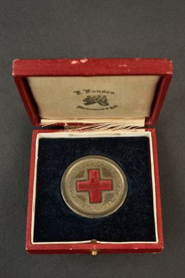 une médaille en forme de croix rouge dans un écrin rouge posé sur un fond noir