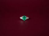 an emerald and diamond ring on a red surface