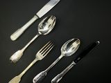 quatre cuillères en argent et un couteau posés sur un plan de travail noir