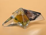 perfume bottle in a pyramid shaped glass holder on a beige surface